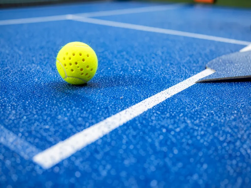 Cận cảnh mặt sân pickleball sơn acrylic xanh có hạt cát, vạch trắng và quả bóng pickleball màu vàng